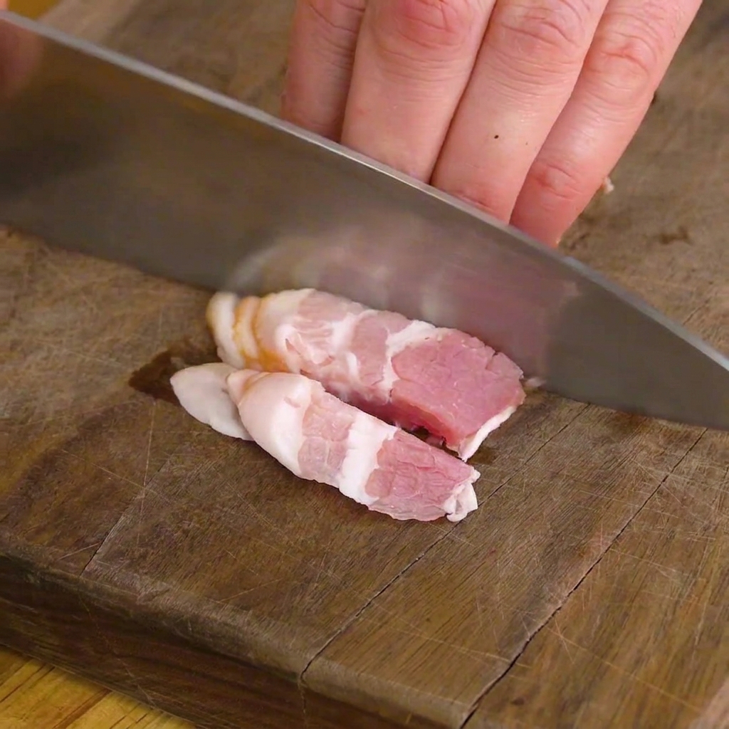 Nahaufnahme von Speckstreifen, die auf einem Holzbrett geschnitten werden.