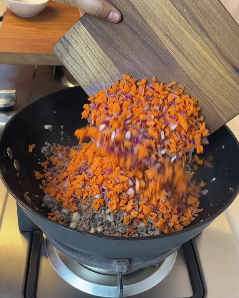 Zerkleinertes Gemüse und gewürfelte Tomaten werden in die Pfanne zum gebratenen Rindfleisch gegeben.