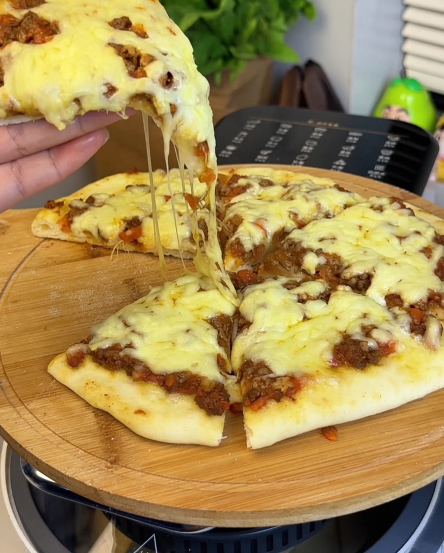 Nahaufnahme der Tomaten-Rinderhack-Sauce, die auf dem Pizzaboden verteilt wird, mit einer Hand, die ein Pizzastück hält.