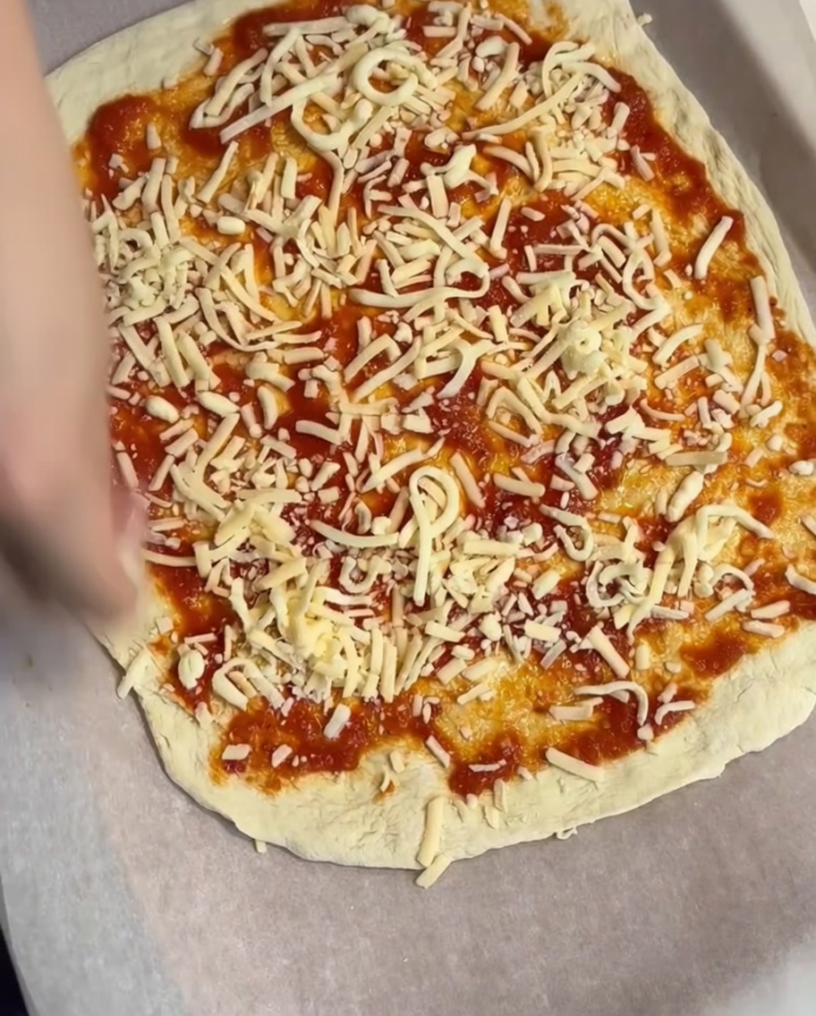 Eine Schicht geriebener Käse wird über den Tomatensaucen-Boden gestreut.