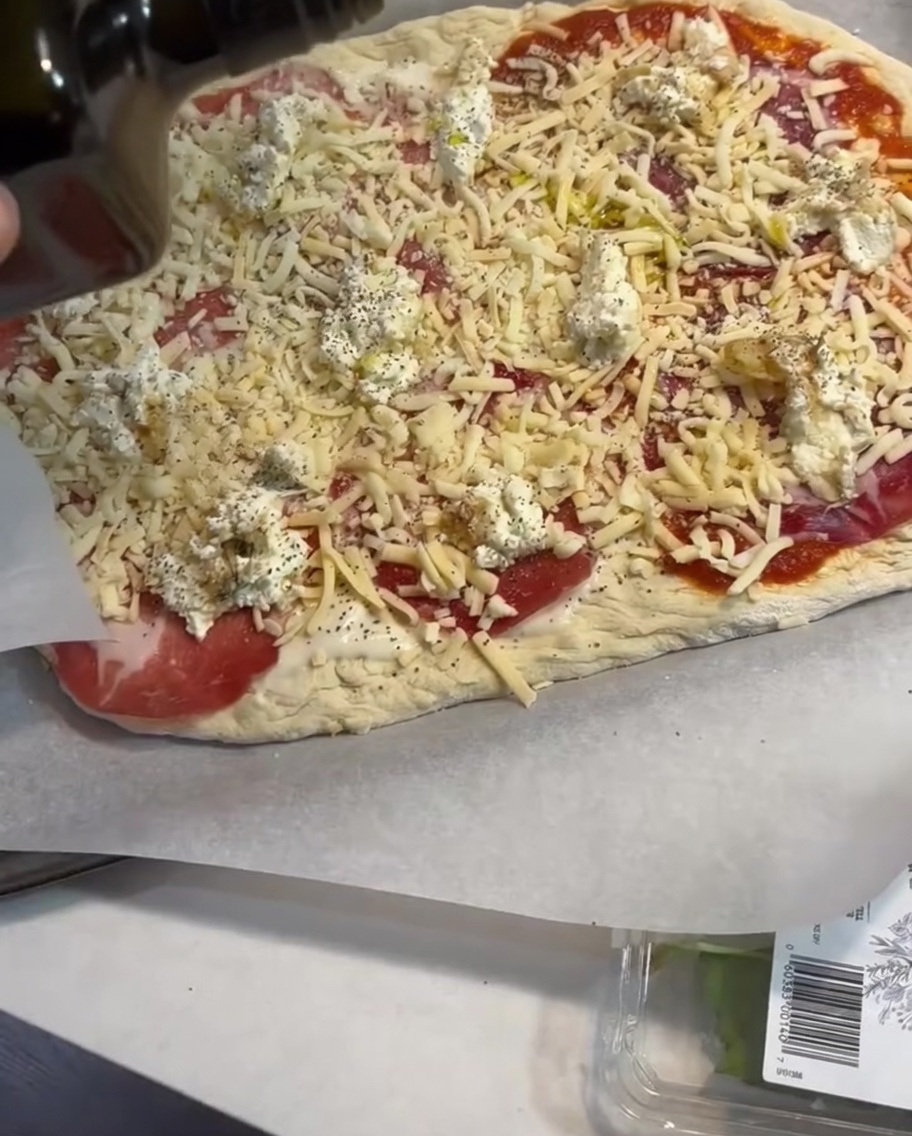 Ein leichter Spritzer Olivenöl wird über die belegte Pizza gegeben.