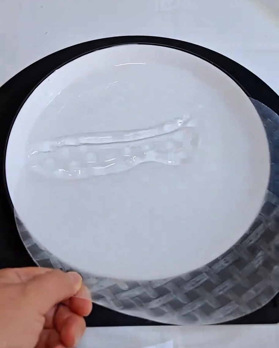 Eine Hand taucht ein trockenes Reispapierblatt in eine Schüssel mit Wasser.