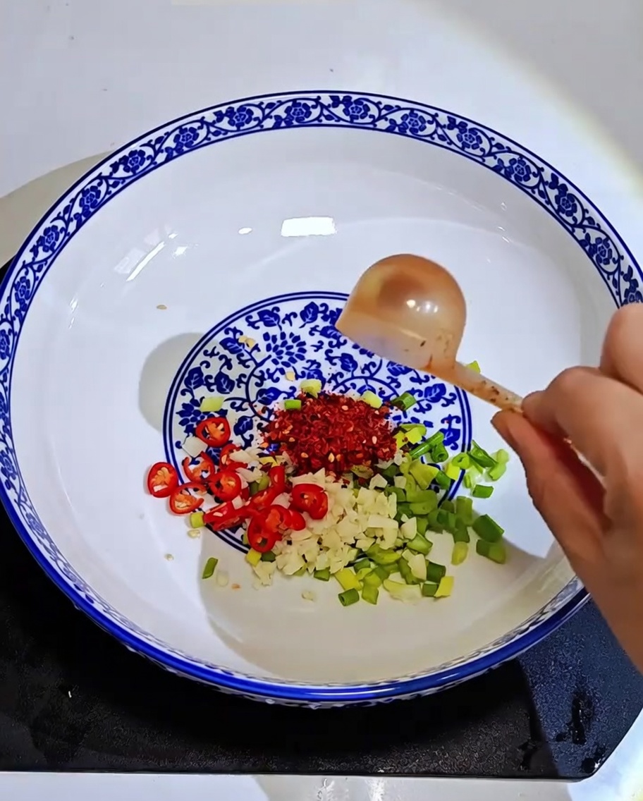 Nahaufnahme von Knoblauch, Frühlingszwiebeln und Chiliflocken, über die heißes Öl gegossen wird.