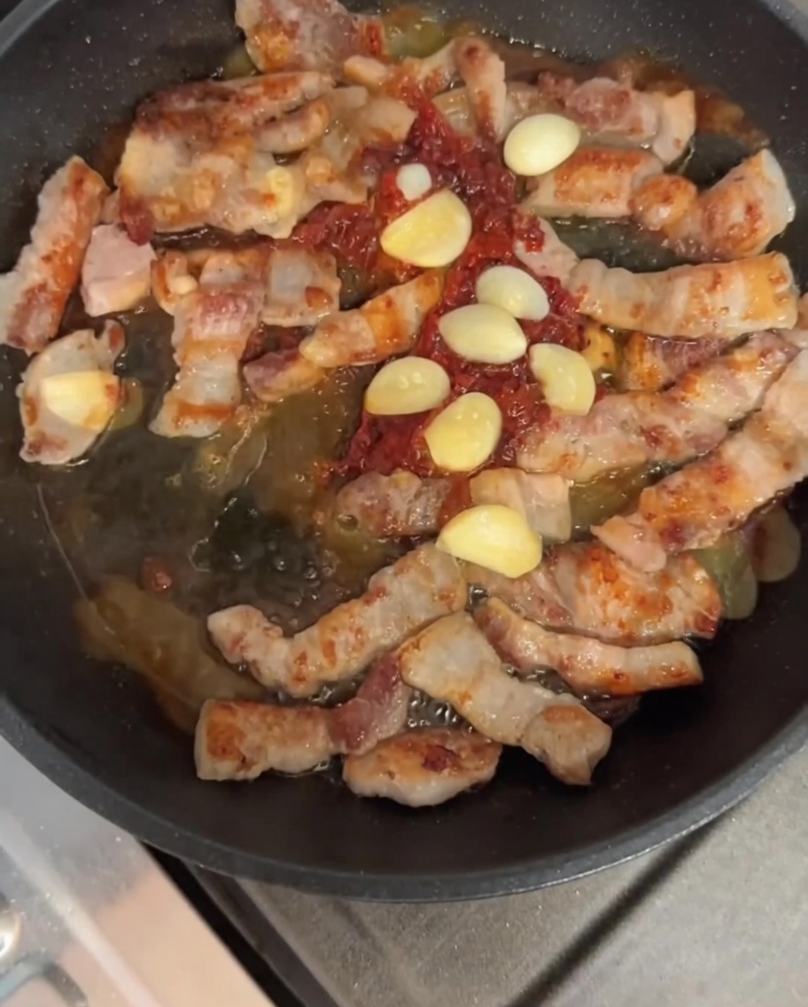 Schweinebauch und Knoblauch werden mit der Soße in der Pfanne pfannengerührt.