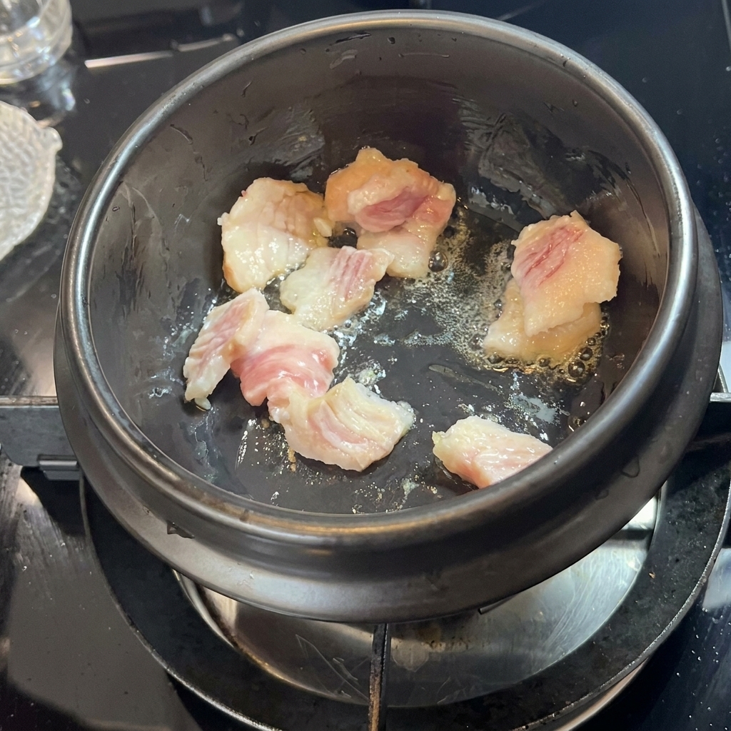 Schweinebauchstücke brutzeln und lassen in einem schwarzen Steintopf Fett aus.