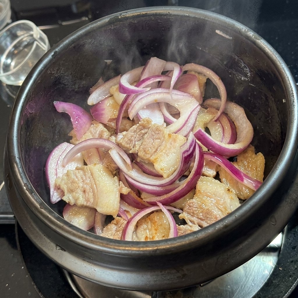 Kimchi vermischt mit Schweinefleisch und Zwiebeln im Steintopf.