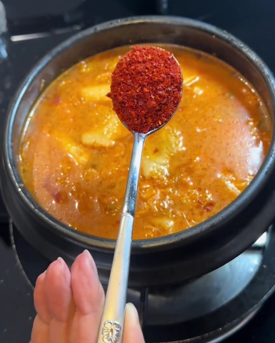 Chilipulver wird mit einem Löffel in den Eintopf gegeben.