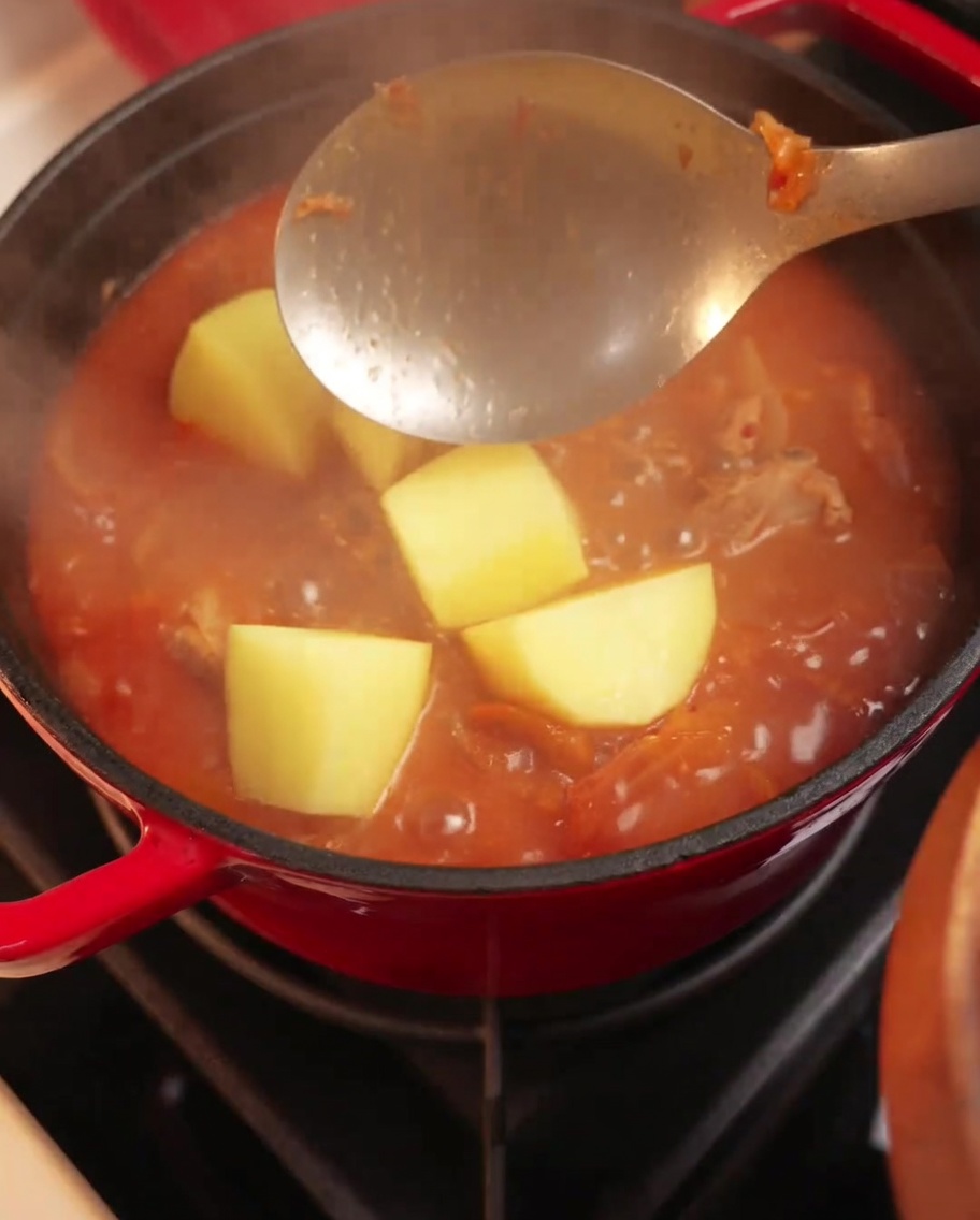 Kartoffelstücke werden in den köchelnden Kimchi-Eintopf gegeben.