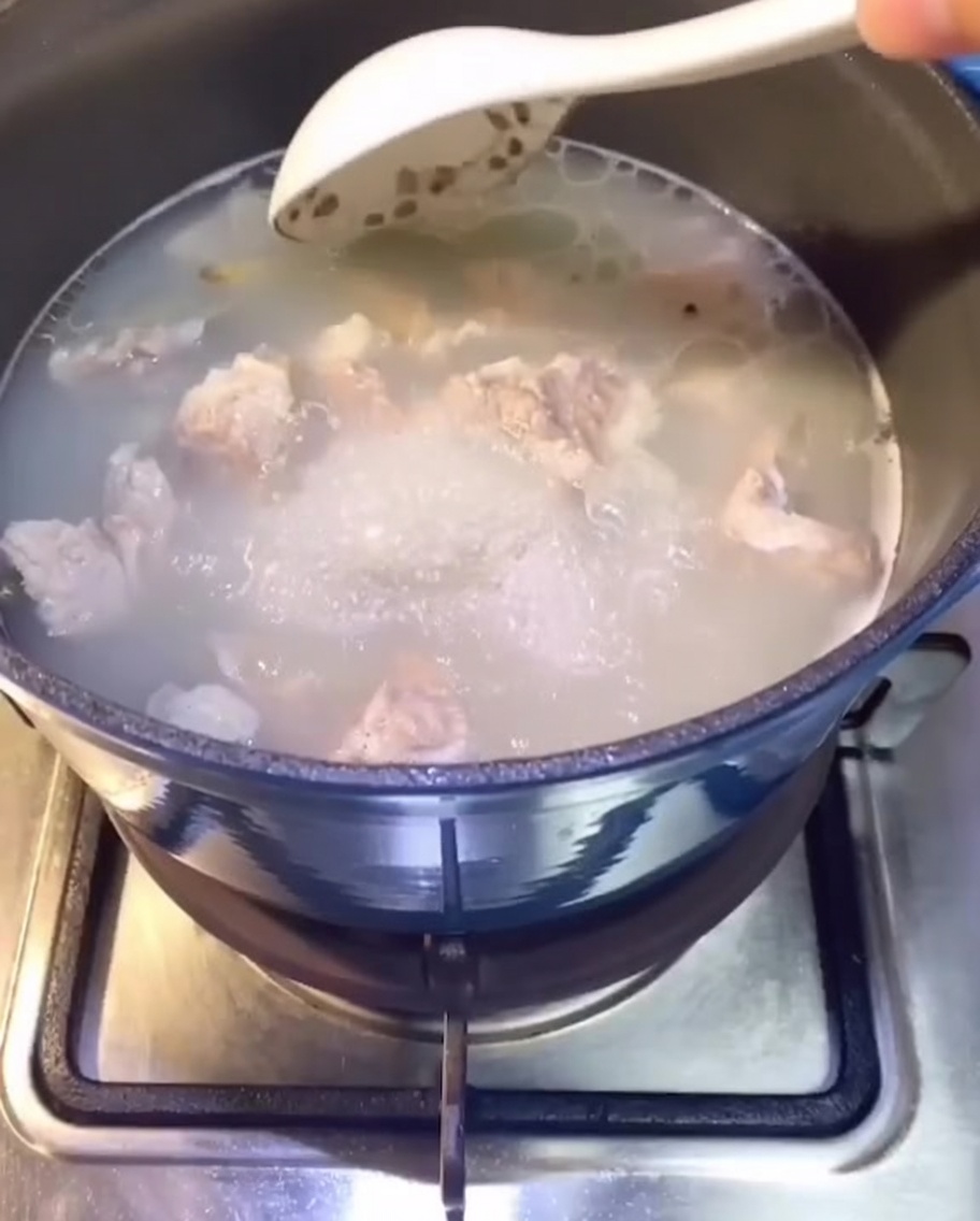 Schweinerippchen kochen in einem Topf mit Wasser auf dem Herd, es bildet sich eine klare Brühe.