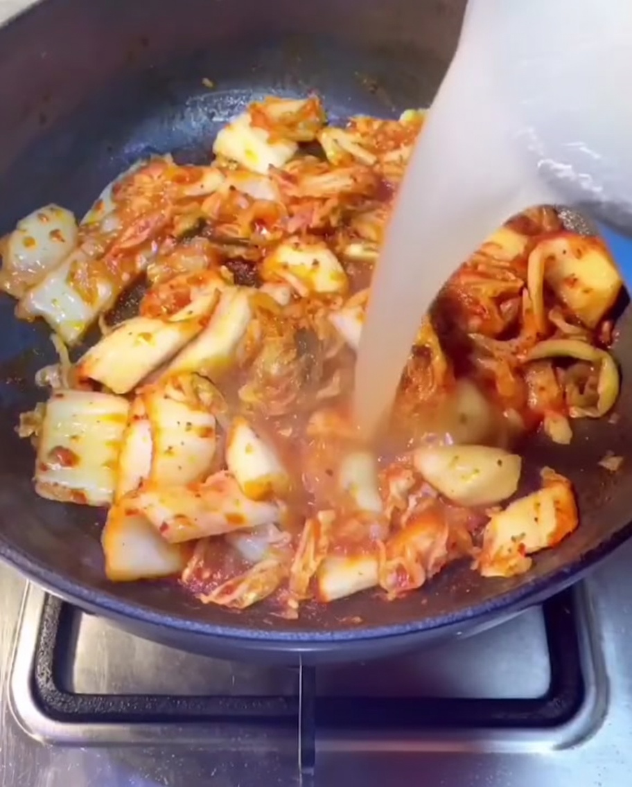 Schweinerippchenbrühe wird in eine Pfanne mit angebratenem Kimchi gegossen.