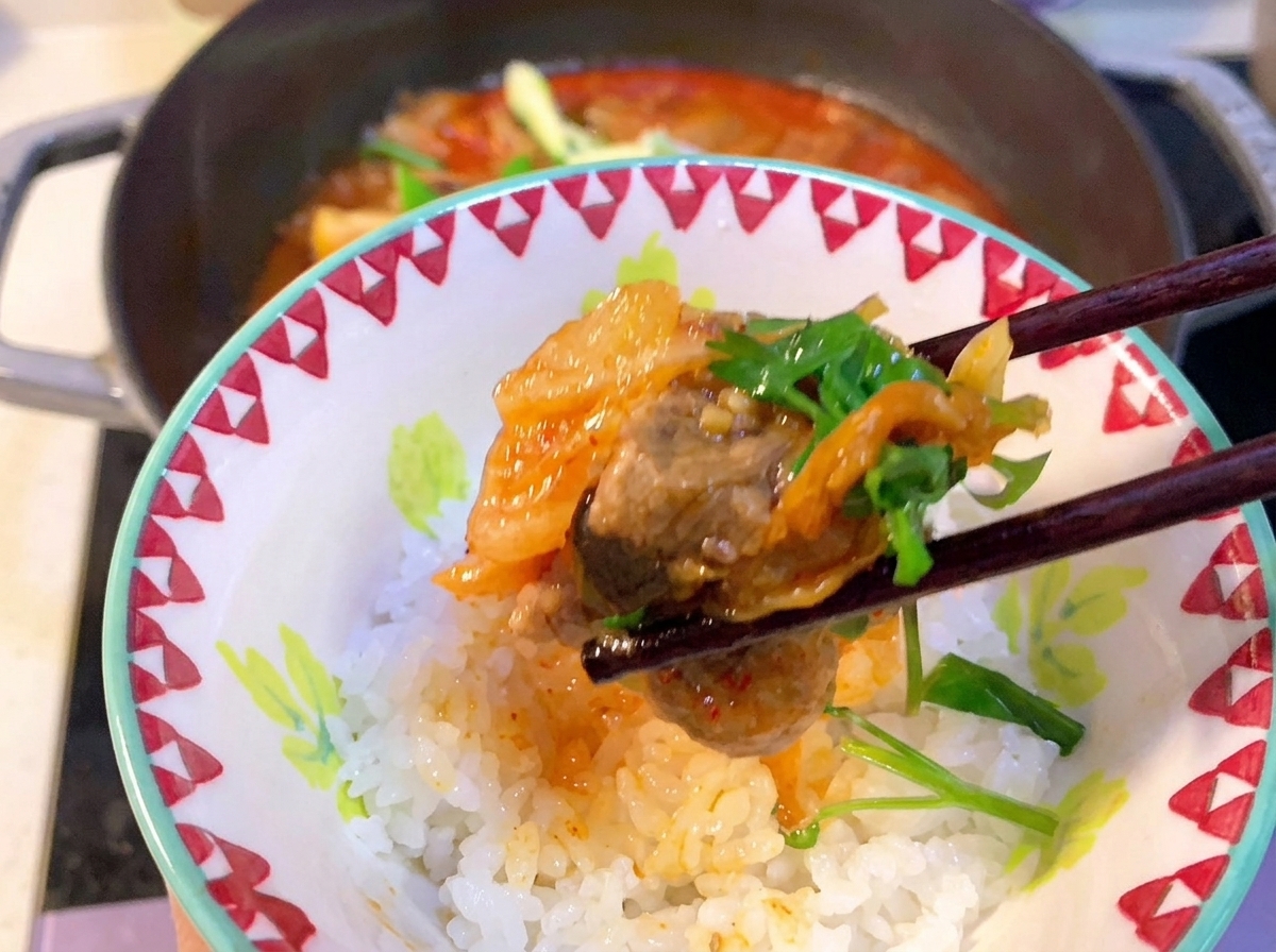 Nahaufnahme eines Löffels, der rote koreanische Chilipaste in den blubbernden Kimchi-Schweinerippchen-Eintopf rührt.