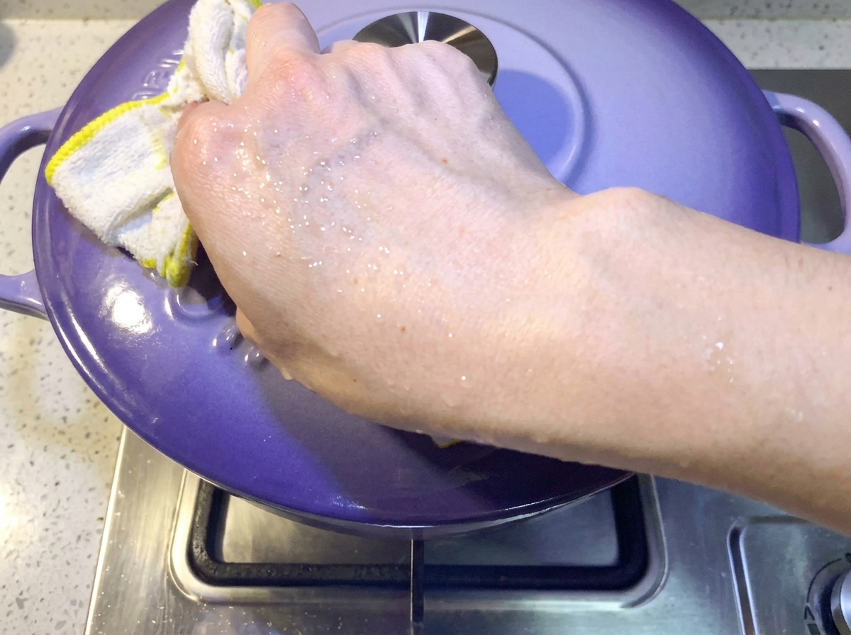Eine Hand legt einen lilafarbenen Deckel auf den Topf, um den Kimchi-Schweinerippchen-Eintopf abzudecken.