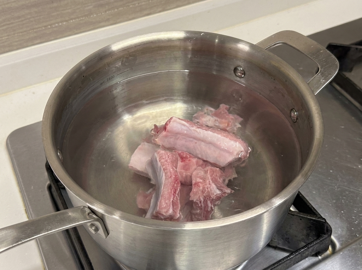 Rohe Schweinerippchen in einem Edelstahltopf mit kaltem Wasser.