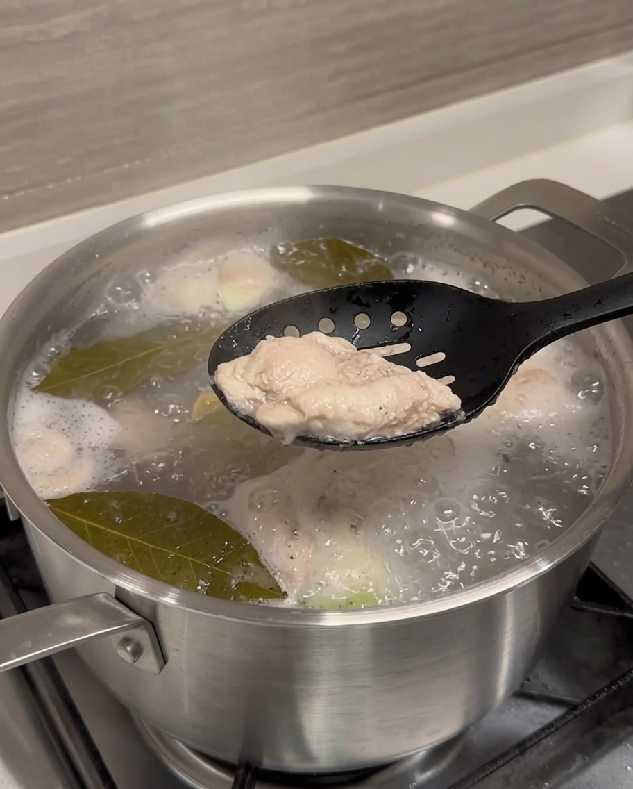 Ein blanchiertes Schweinerippchen wird mit einer Zange aus kochendem Wasser gehoben.