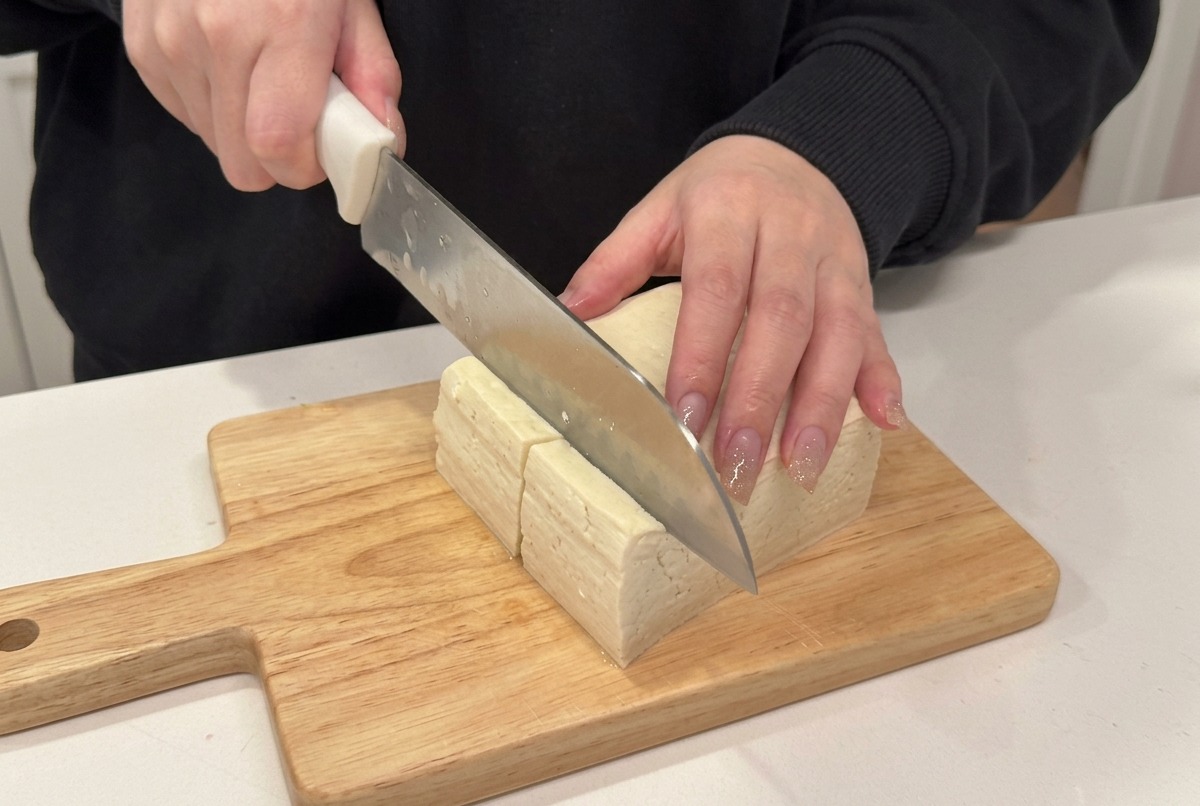 Ein Block weicher Tofu wird in Würfel geschnitten.