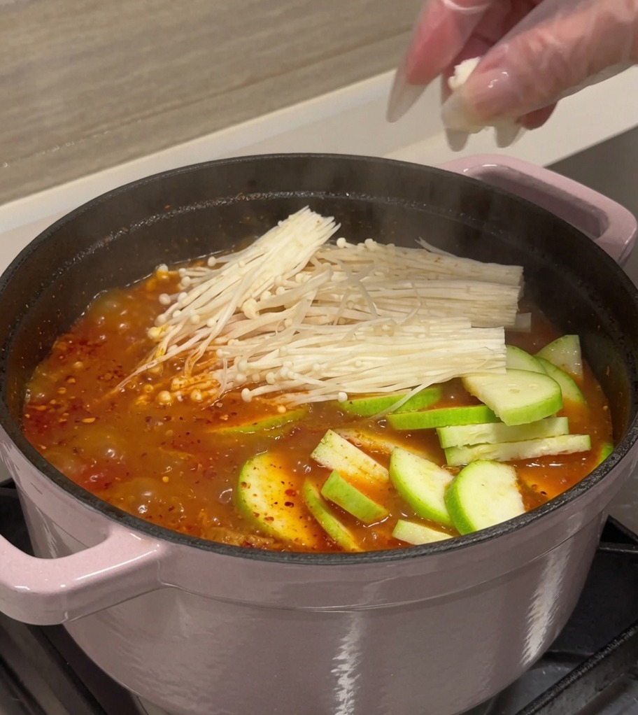 Zucchini, Tofu und Enoki-Pilze werden in die kochende Brühe gegeben.