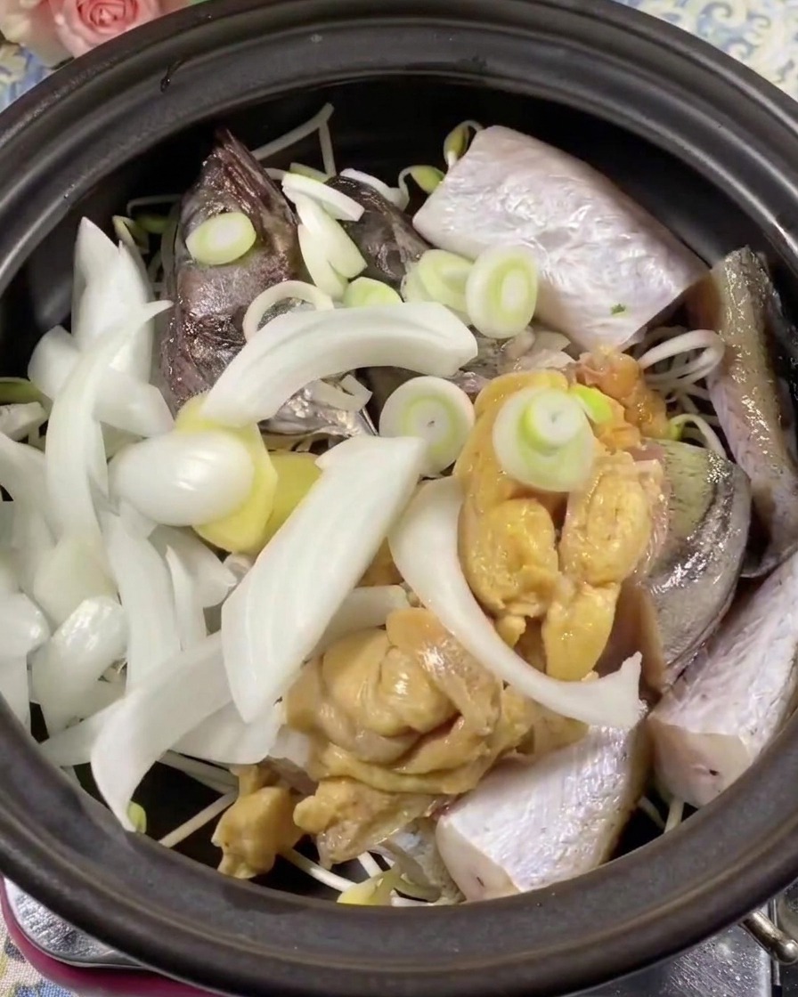 Nahaufnahme von grünen und roten Chilischeiben, die auf Fisch und Zwiebeln im Tontopf verteilt werden.