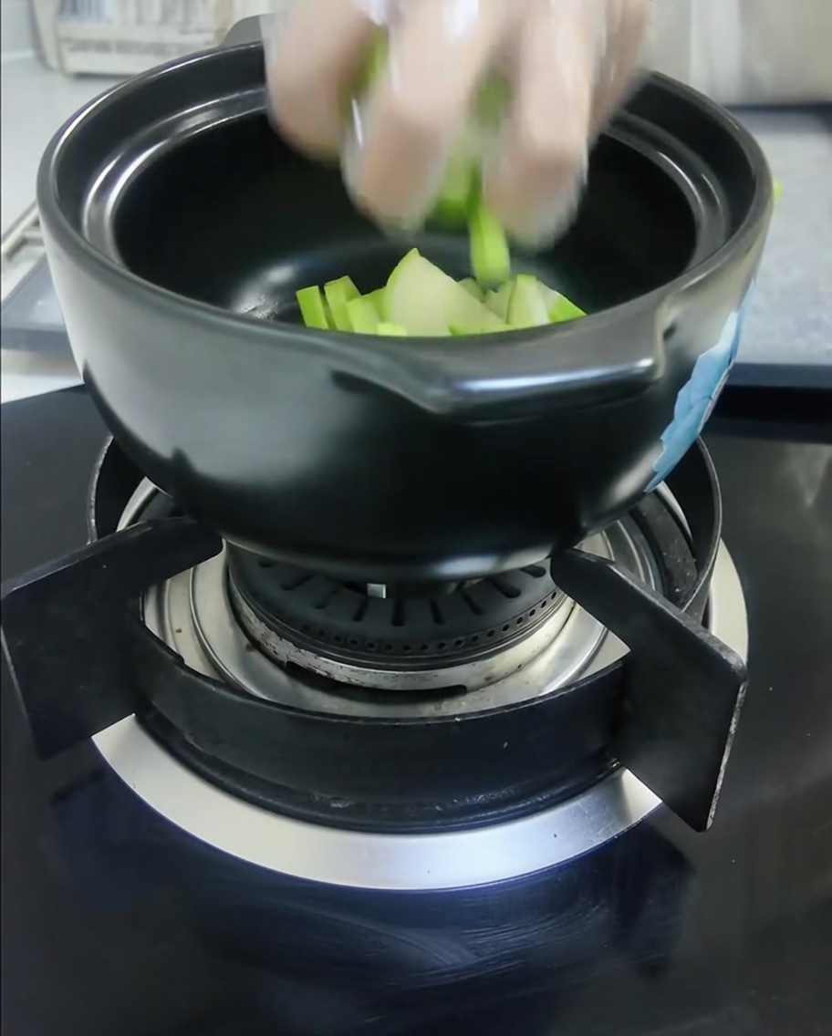 Gewürfelter grüner Squash und geschnittene weiße Zwiebeln in einem schwarzen Tontopf.