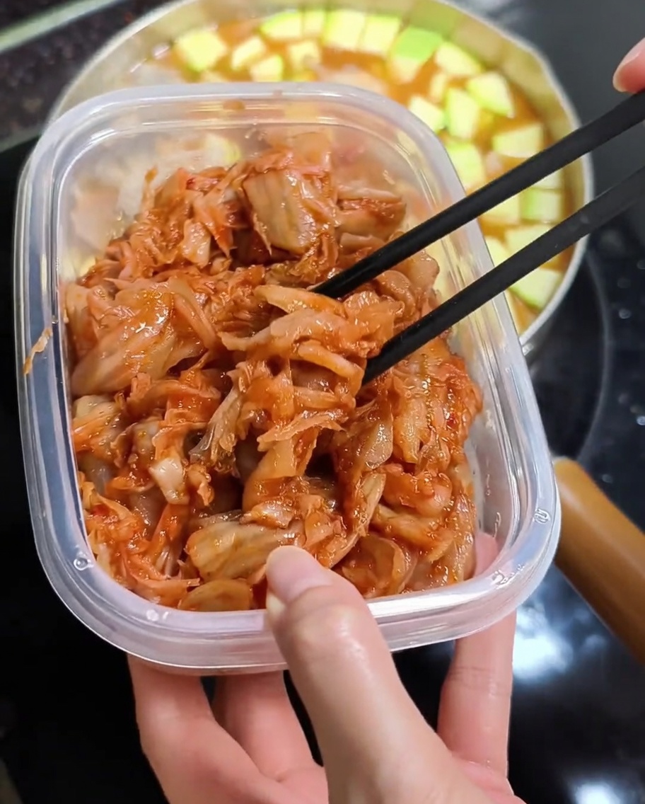 Gehacktes Kimchi wird in den Eintopf gegeben.