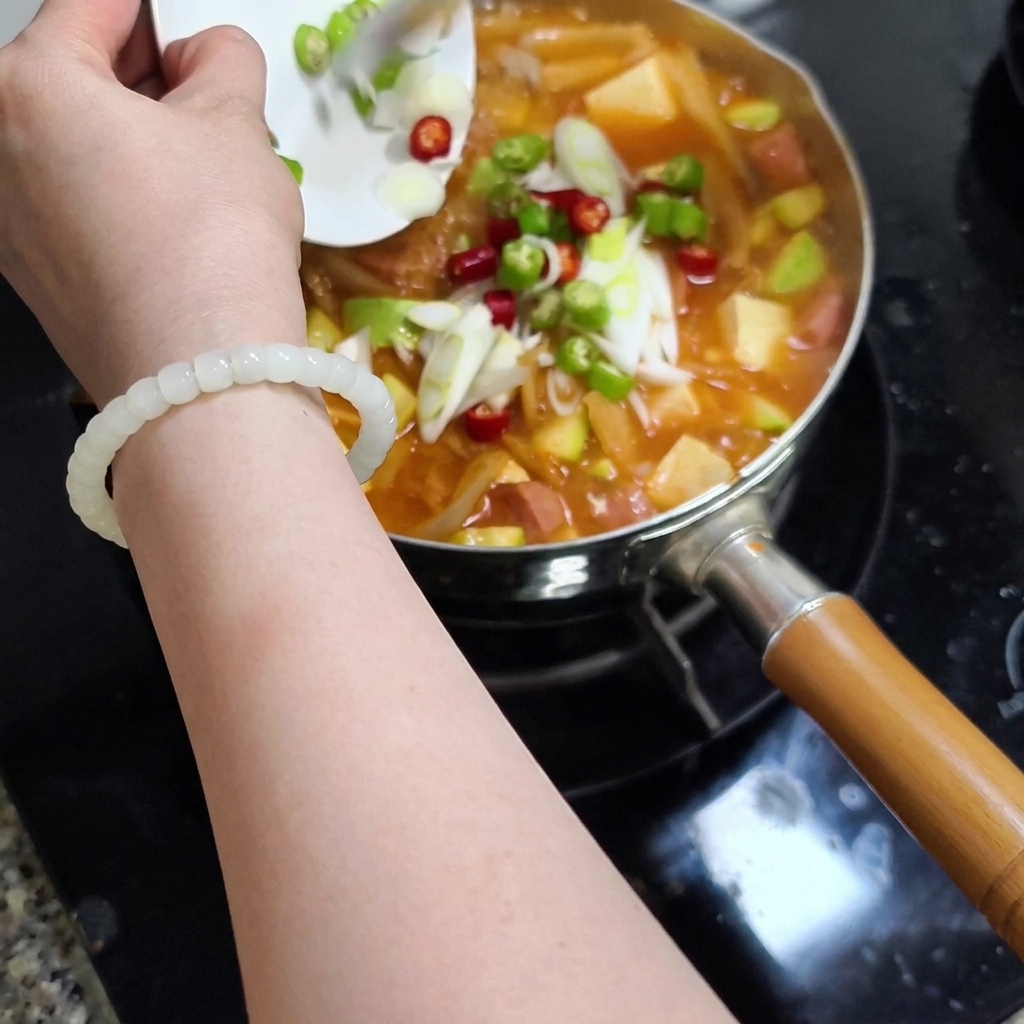 Chilischoten und Frühlingszwiebeln werden in den Topf gegeben.
