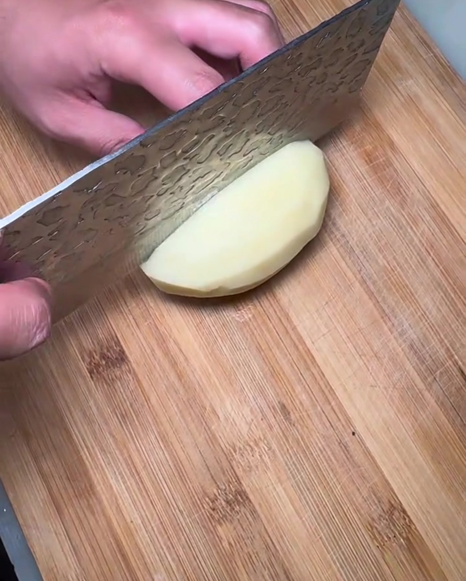Geschälte und in gleichmäßige Scheiben geschnittene Kartoffeln auf einem Holzbrett.