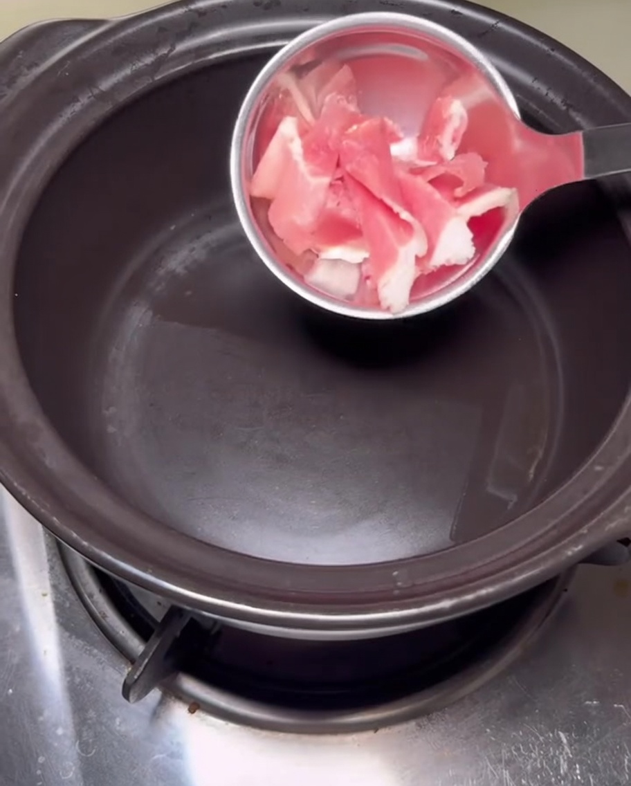 Schweinebauchscheiben, die in einem schwarzen Tontopf angebraten werden.