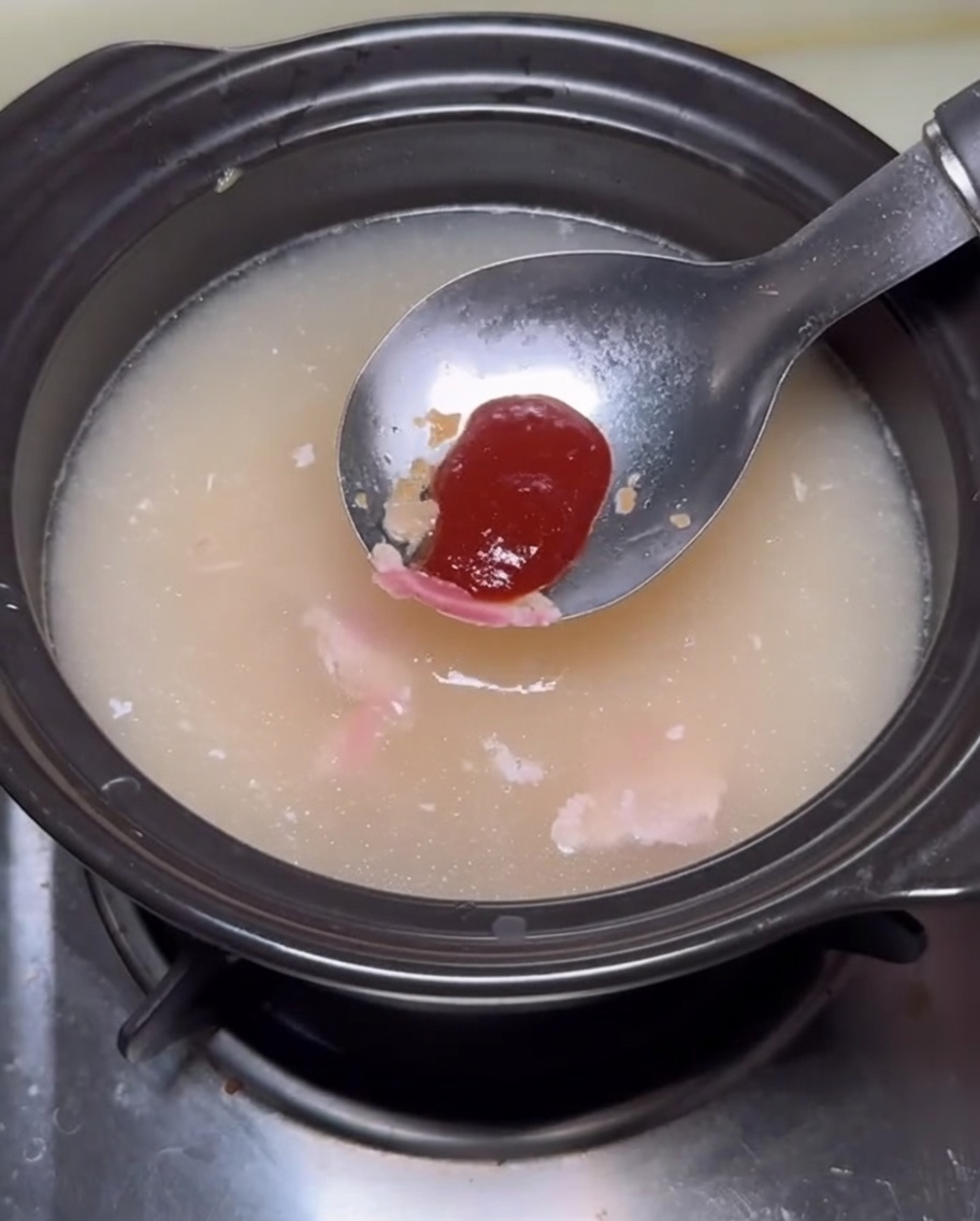 Ein Löffel mit rötlicher Sauce wird in den Eintopf gegeben.