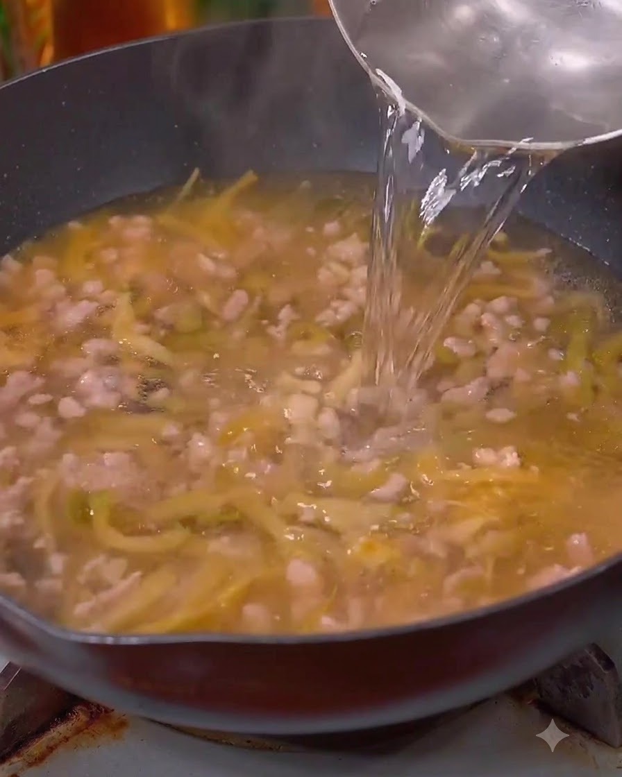 Wasser wird aus einer Karaffe in den Wok über das Fleisch und den Kohl gegossen.