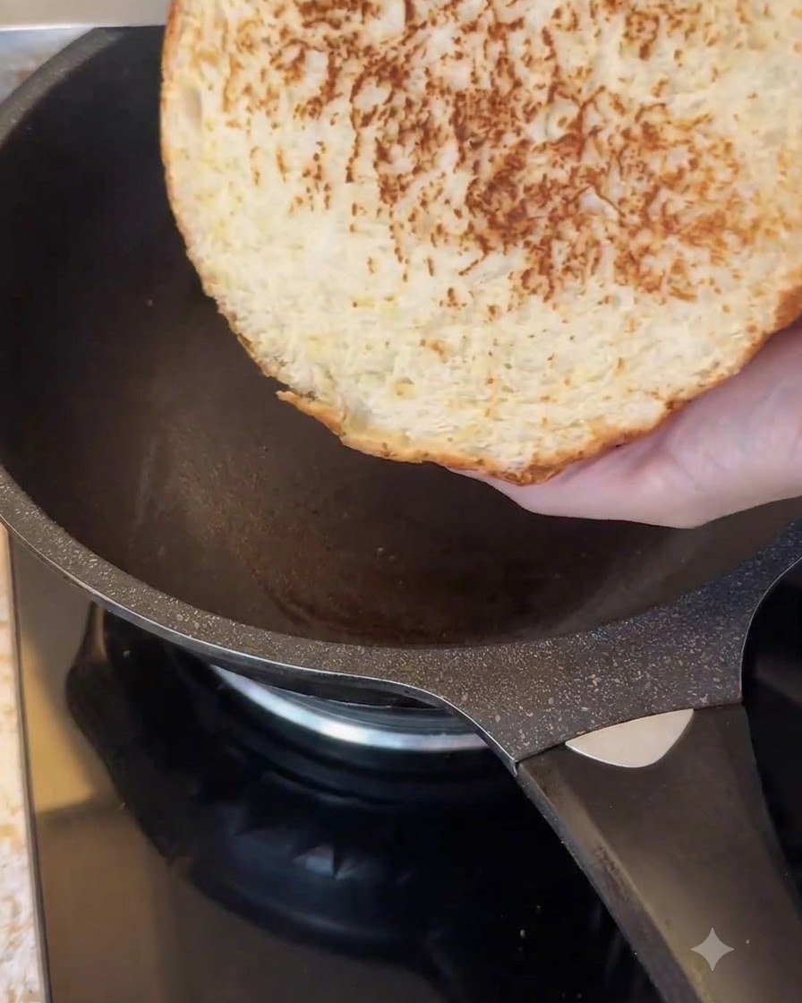 Die Schnittseite eines großen Burgerbrötchens wird in einer dunklen Antihaft-Bratpfanne getoastet.