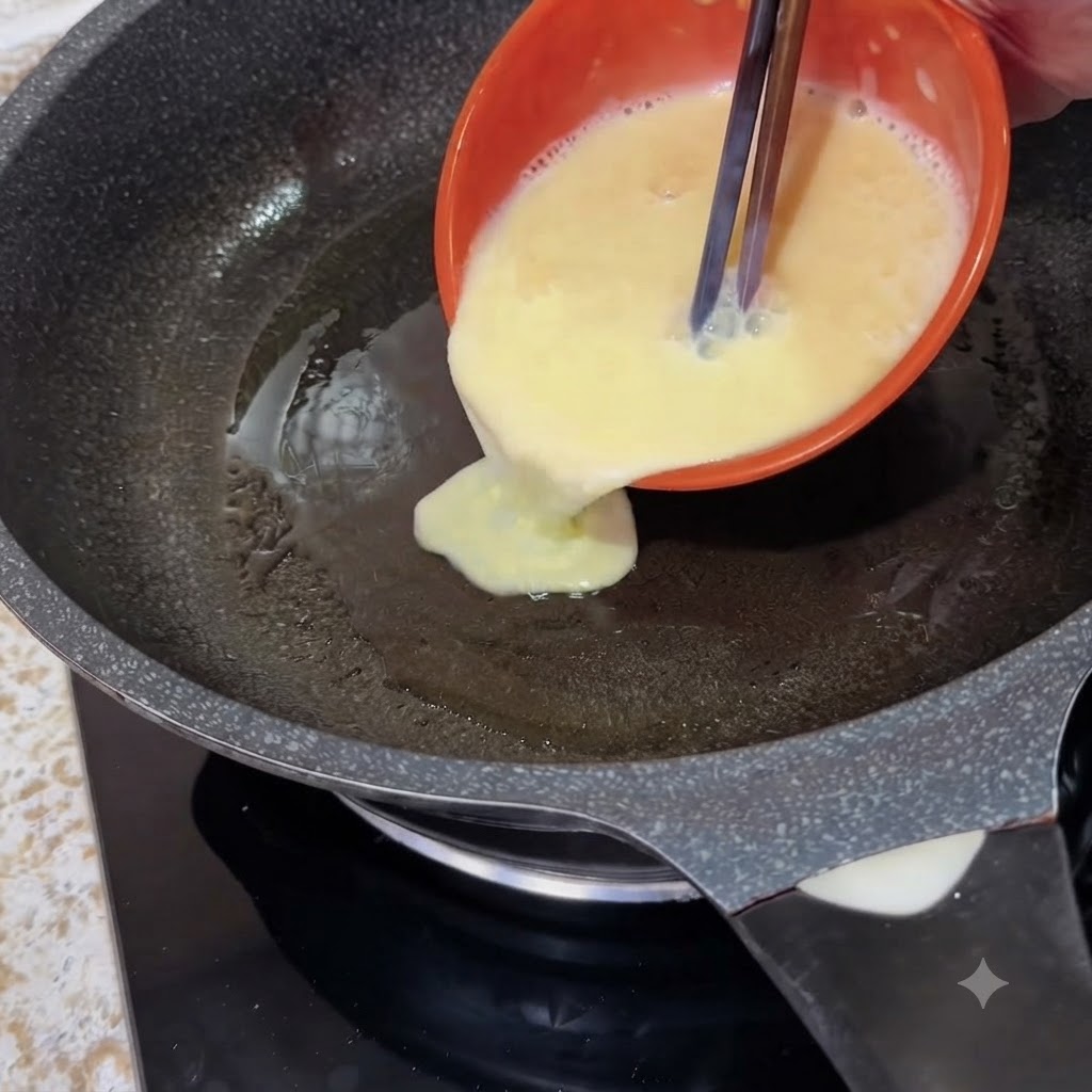 Eine orangefarbene Schüssel gießt flüssige geschlagene Eier mit Stäbchen in eine heiße Bratpfanne.