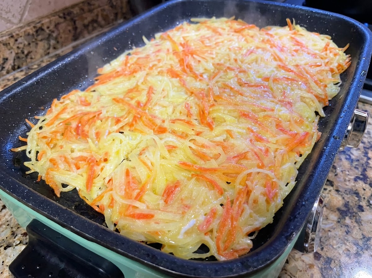 Ein großer Kartoffelrösti wird in der Pfanne mit Pfannenwendern in kleinere Portionen geschnitten.