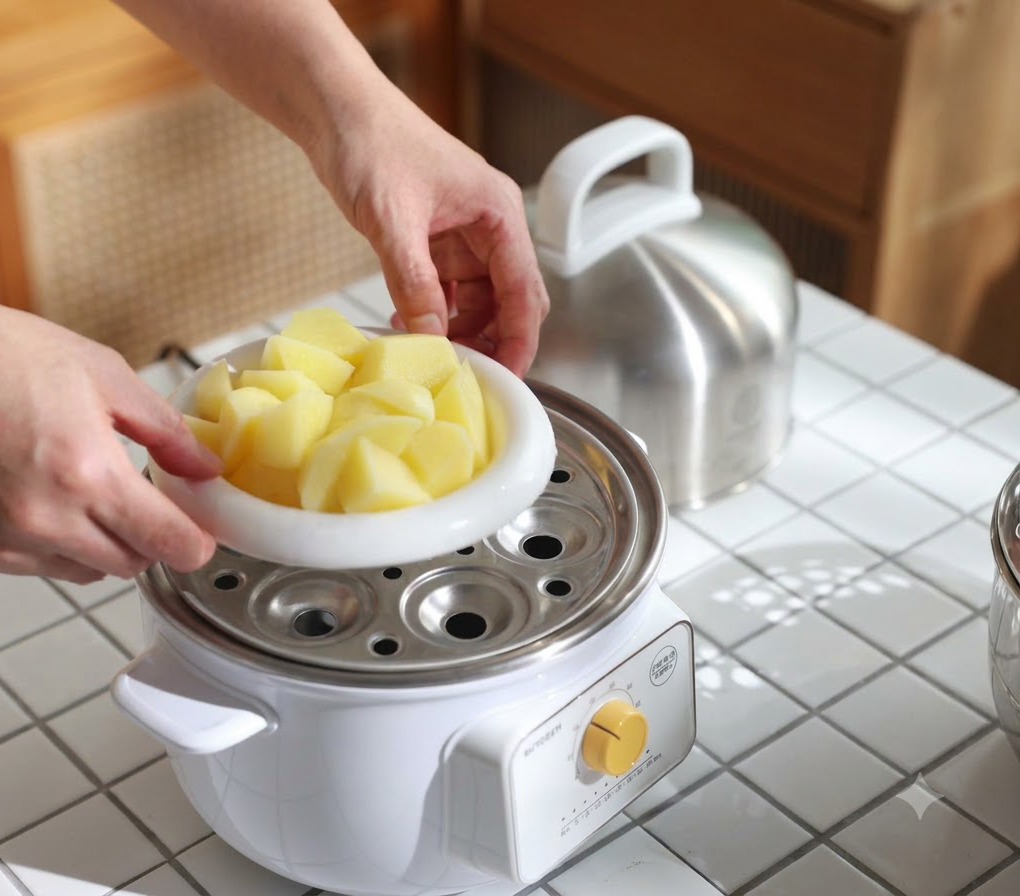 Eine weiße Schüssel gefüllt mit Kartoffelstücken wird in einen Dämpftopf gestellt, um sie weich zu garen.