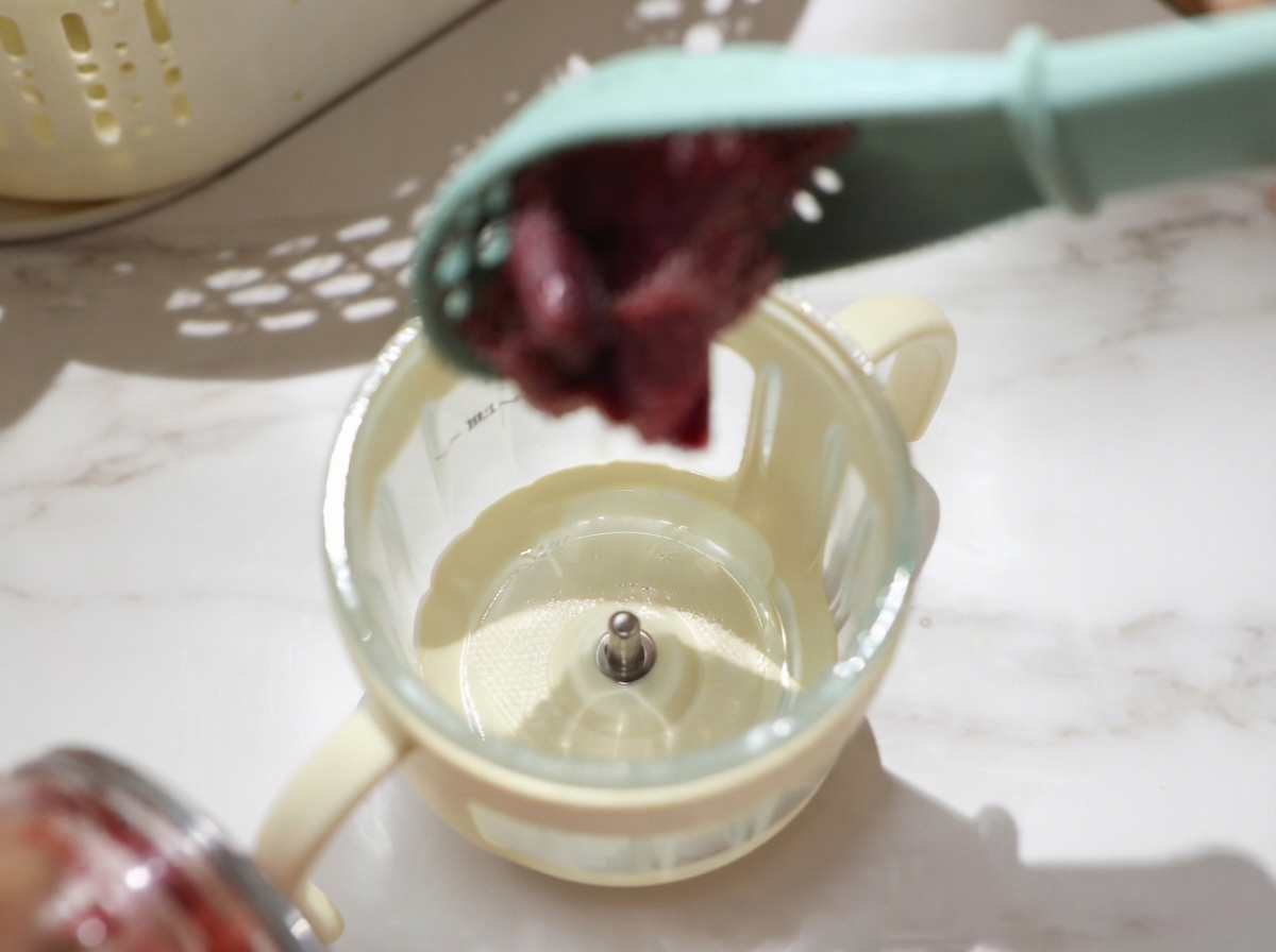 Abgetropfte Stücke rohen Rindfleischs werden mit einem Löffel in den kleinen Mixbecher eines Zerkleinerers gefüllt.