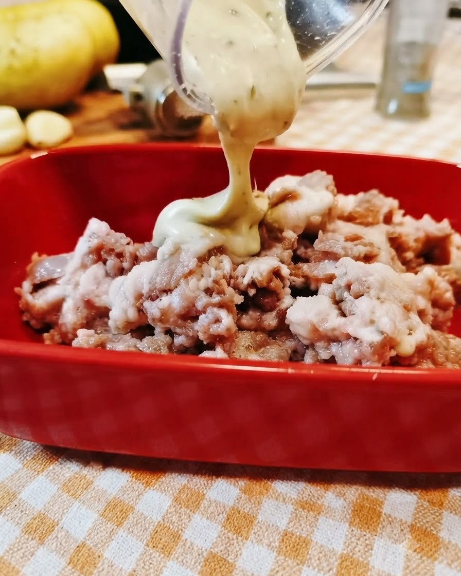 Sauce wird aus einem klaren Behälter in eine rote Schüssel mit gewürztem Hackfleisch gegossen.