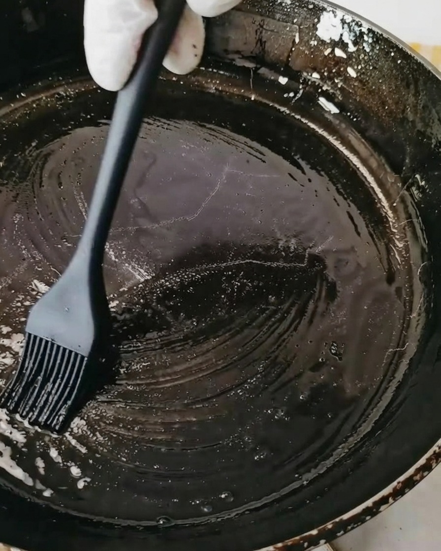 Eine schwarze Pfanne wird mit einem Silikonpinsel mit Öl bestrichen.