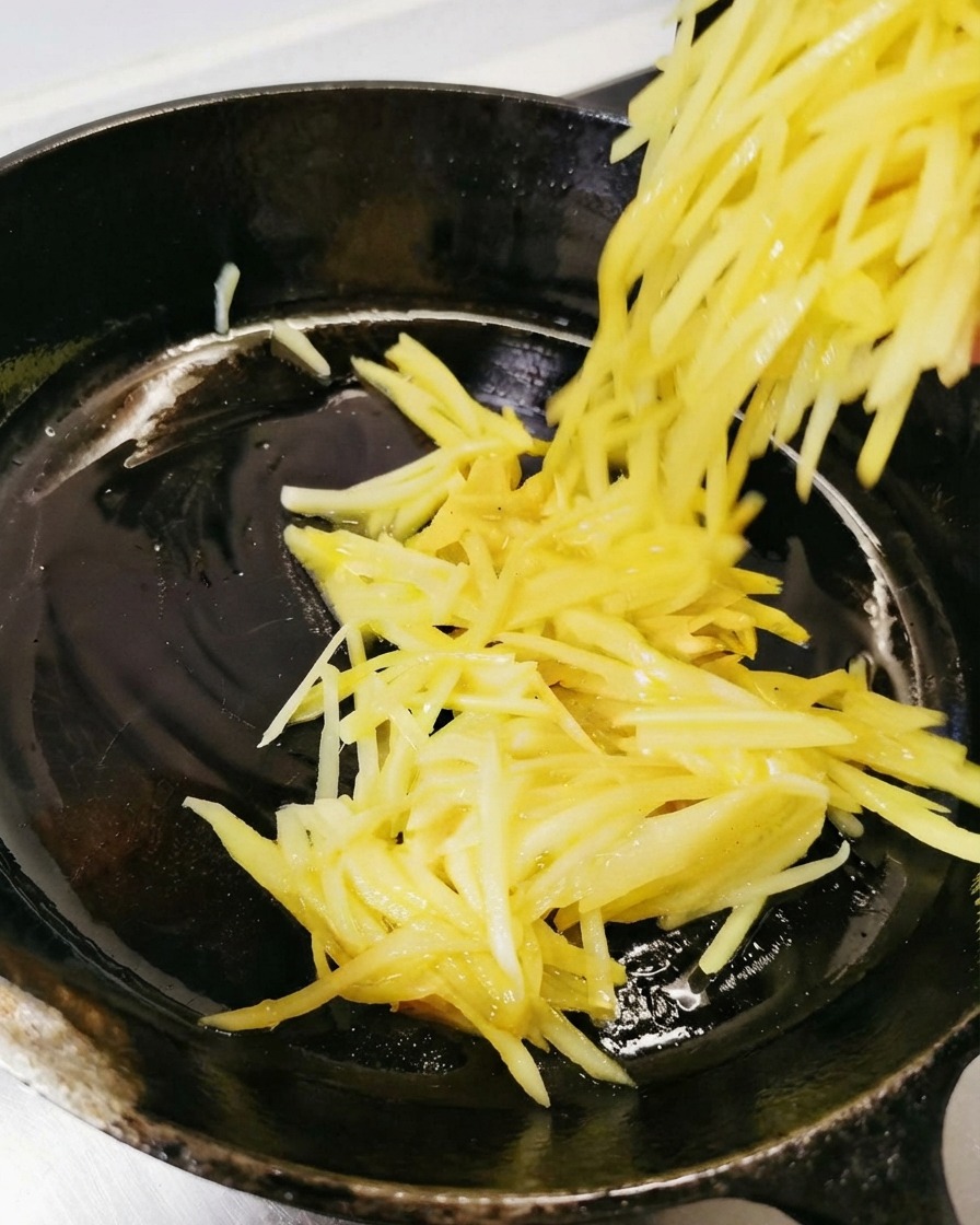 Geriebene Kartoffeln werden in die geölte schwarze Pfanne gefüllt und verteilt.