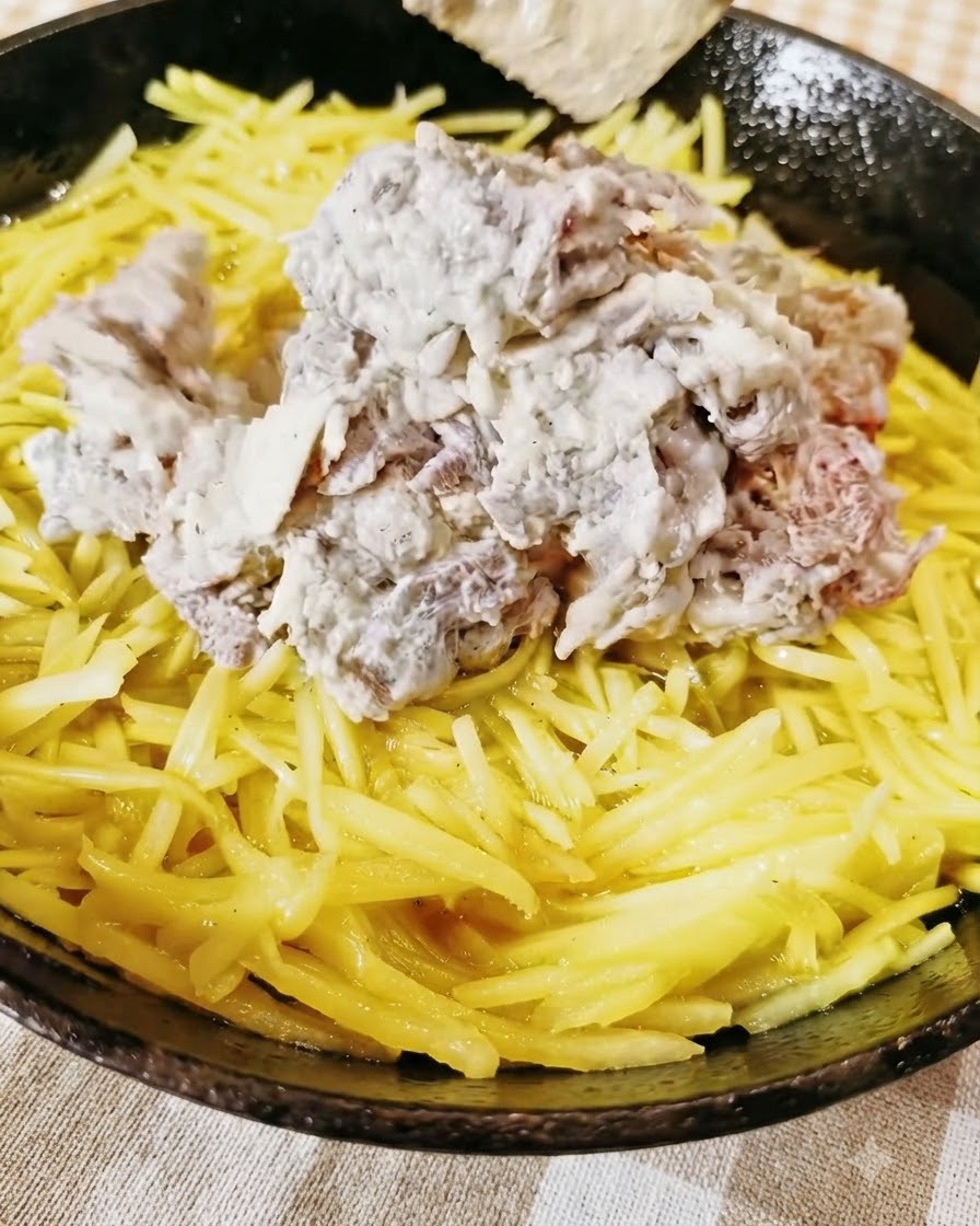Gewürztes Hackfleisch auf einer gelben Schicht Kartoffelraspeln in einer Pfanne.