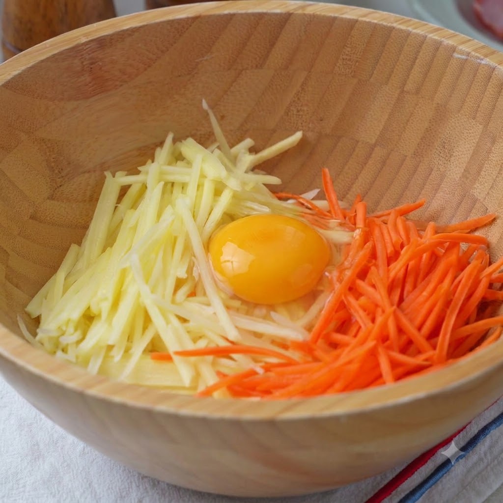 Eine Holzschüssel gefüllt mit geriebenen Kartoffeln, Karotten, einem Ei, Mehl, Salz und Pfeffer, bereit zum Mischen.