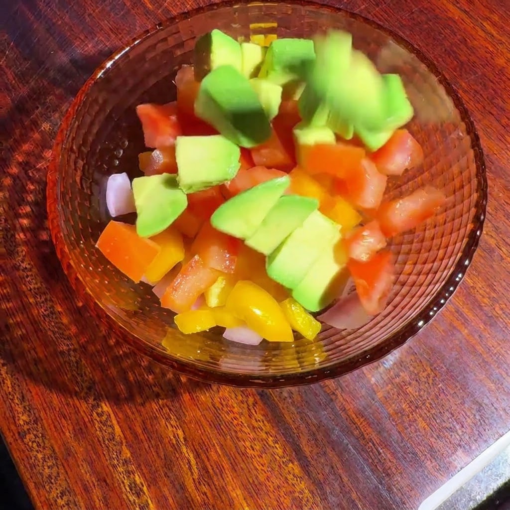 Gewürfeltes Gemüse und Avocado werden in einer Glasschüssel mit Dressing vermengt.