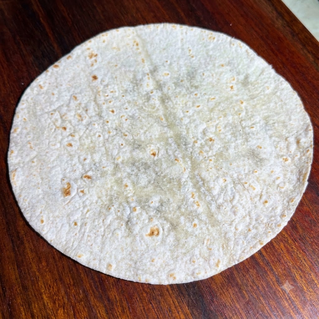 Frische grüne Salatblätter, ordentlich auf einer flachen, runden Vollkorn-Tortilla angerichtet.