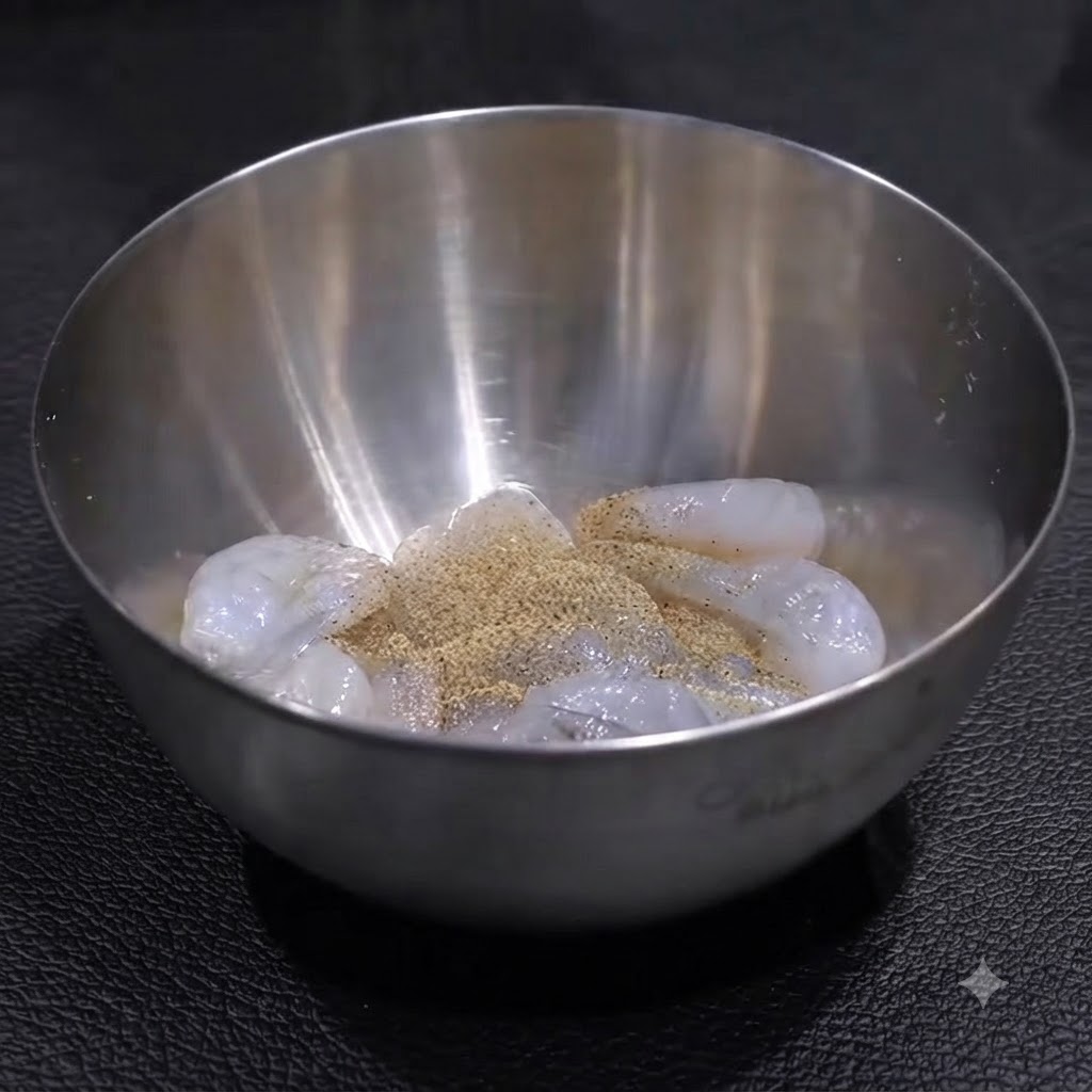 Rohe Garnelen in einer Edelstahlschüssel, gewürzt mit einer Schicht Pfeffer und Salz, bereit zum Mischen.