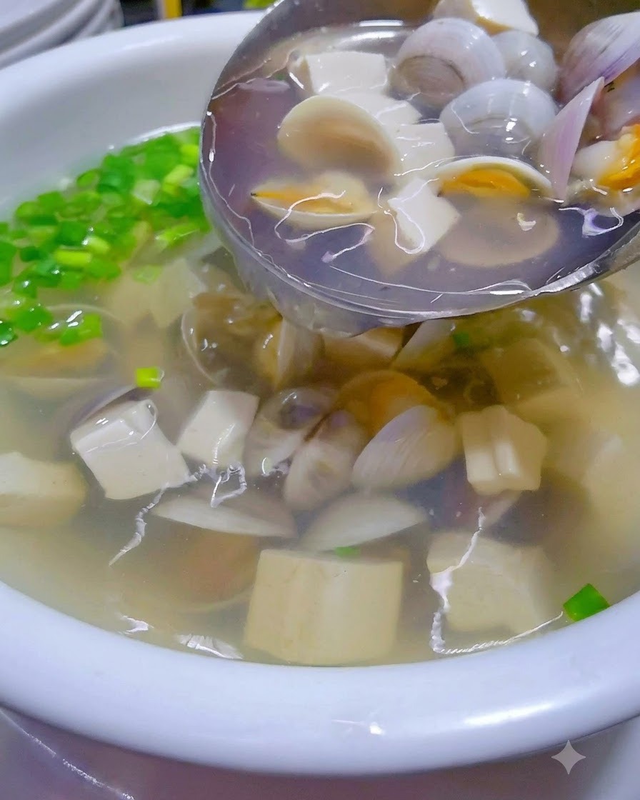 Heiße Muschel-Tofu-Suppe wird aus einem Wok in eine garnierte Servierschüssel gegossen.
