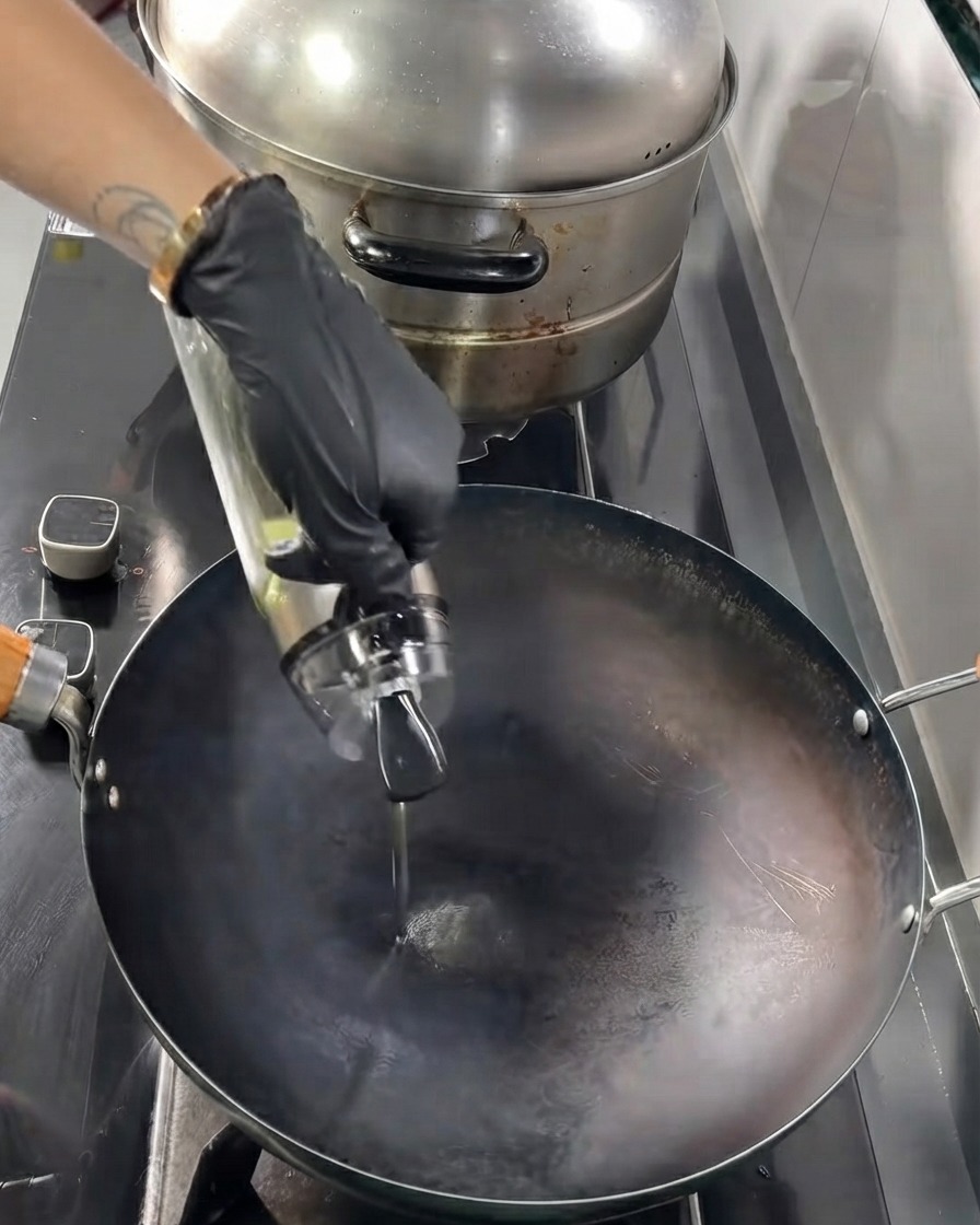 Speiseöl wird aus einer Glasflasche in einen heißen schwarzen Wok gegossen.