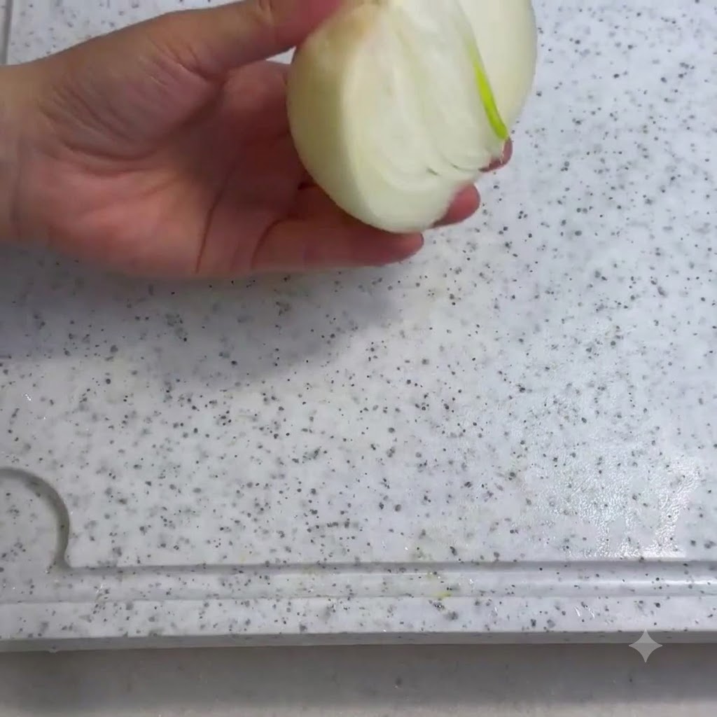 Eine geschälte Zwiebel wird auf einem weißen Schneidebrett mit einem Messer geschnitten.