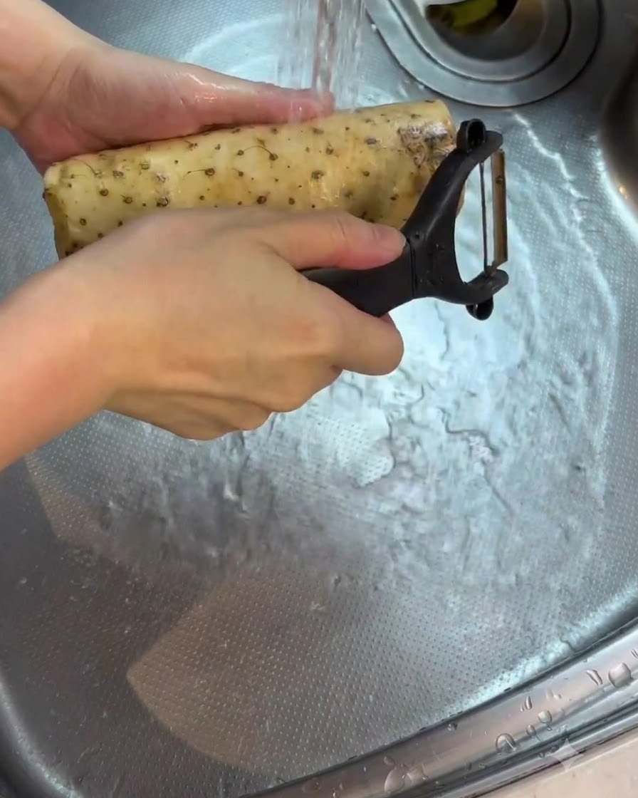 Eine geschälte Yamswurzel wird im Waschbecken unter fließendem Wasser abgespült und gereinigt.