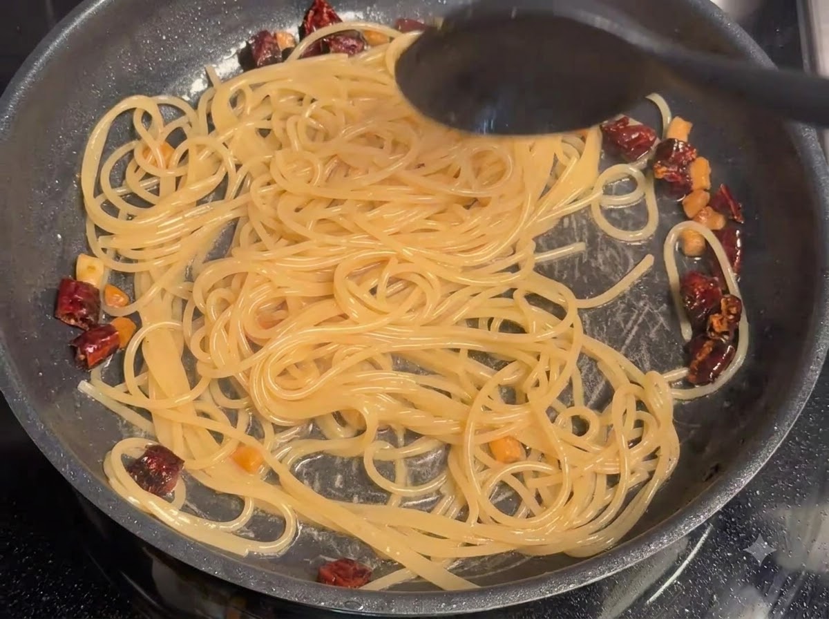 Nudelwasser wird in Spaghetti und Fleisch in einer Pfanne eingerührt.