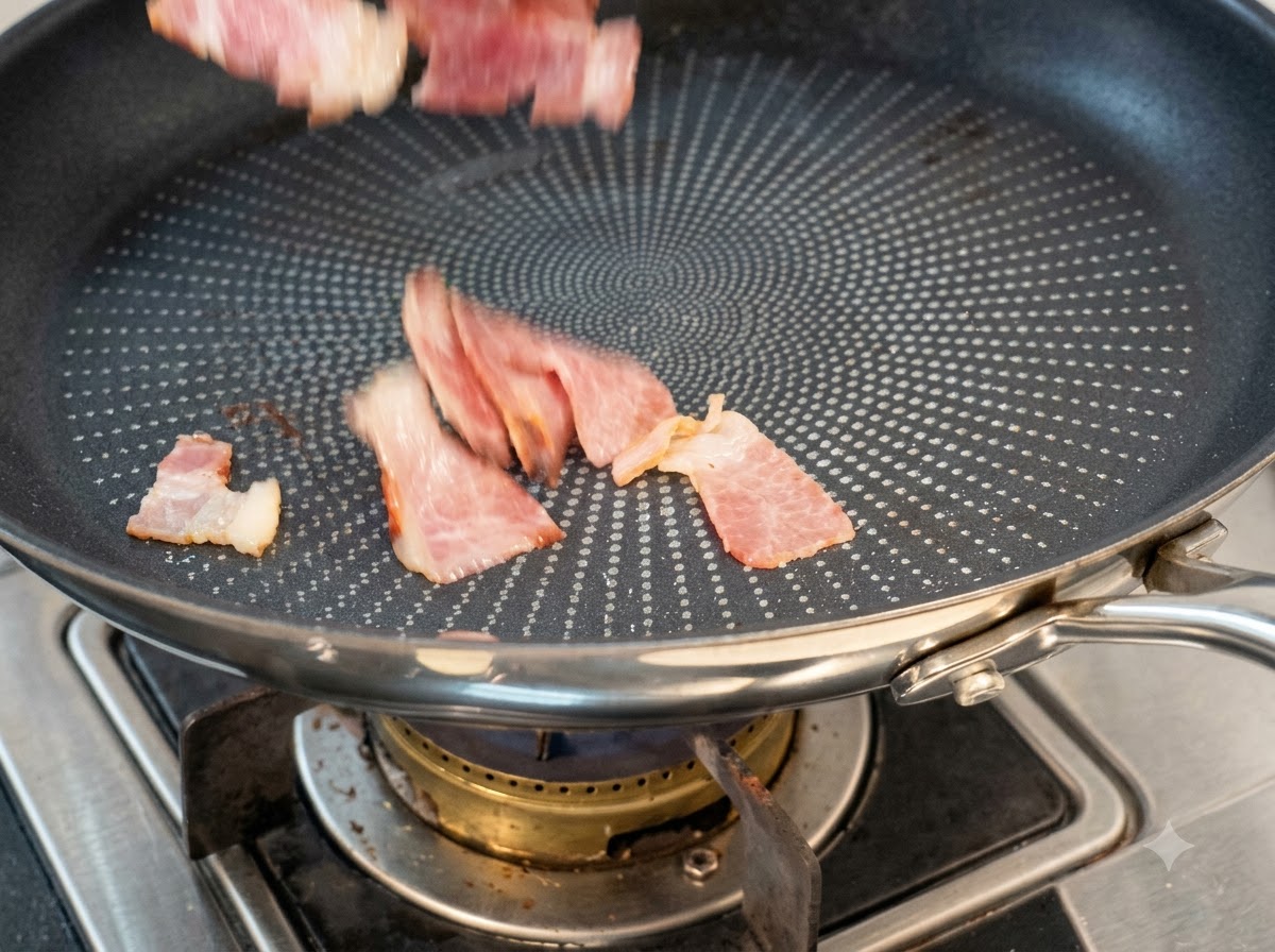 Sliced bacon pieces being dropped into a dry non-stick frying pan to cook.