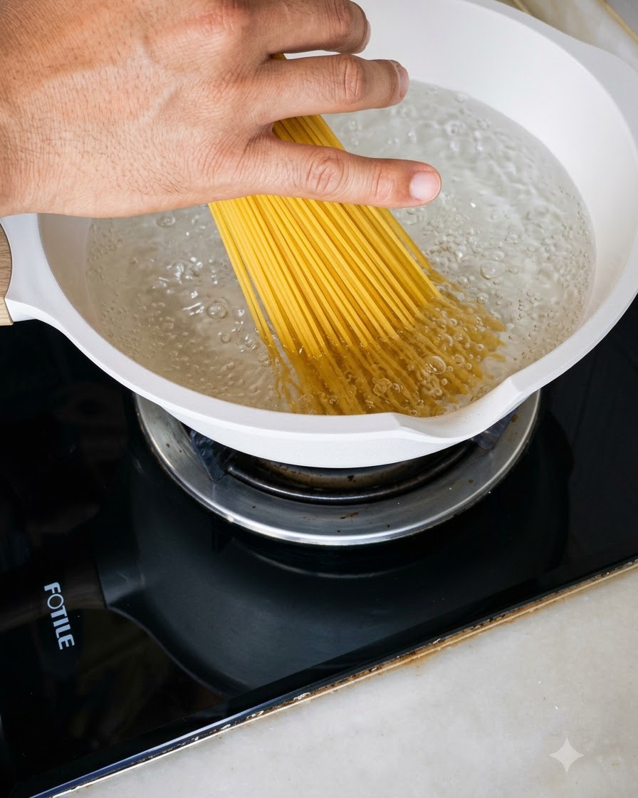 Eine Handvoll trockener Spaghetti wird in einen weißen Topf mit sprudelnd kochendem Wasser gegeben.