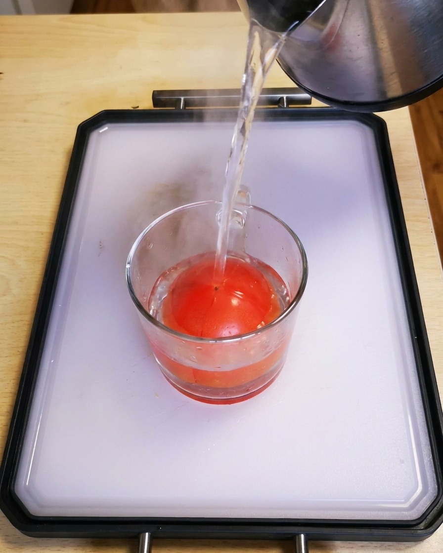 Heißes Wasser wird aus einem Wasserkocher in ein Glas mit einer frischen roten Tomate gegossen.