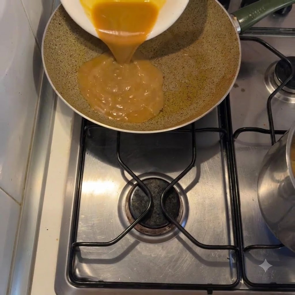 Dickflüssige goldene Sauce wird von einem weißen Teller in eine Bratpfanne auf einem Herd gegossen.